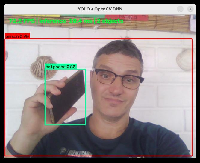 A person detected by YOLO holding a cell phone, both boxed and labelled by the detector
